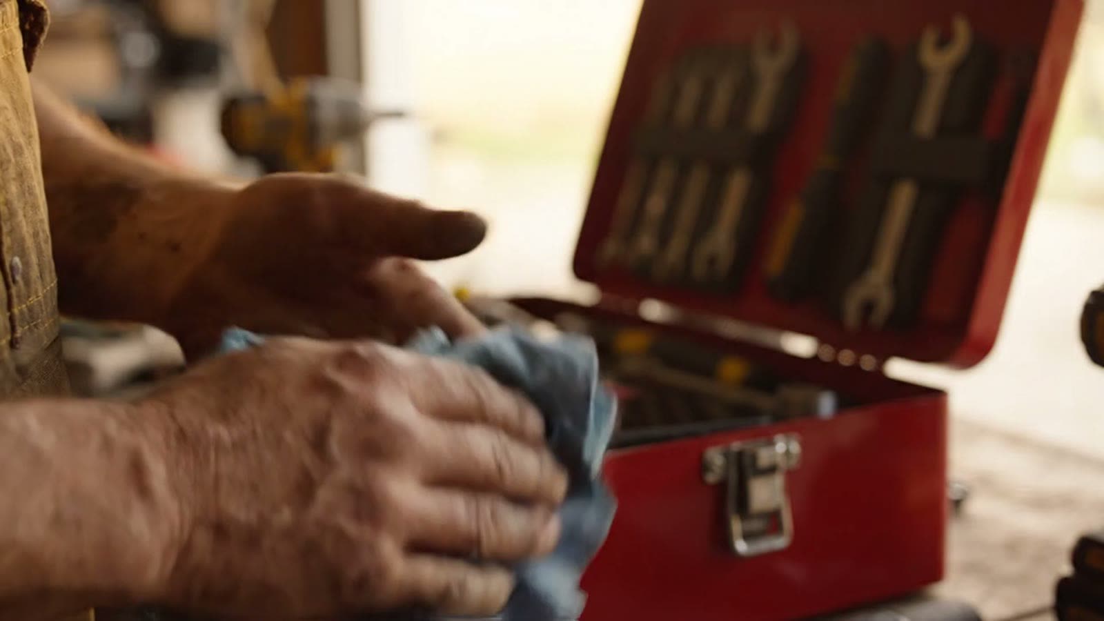 A tradesman’s hands at an open red toolbox of wrenches on a work surface.