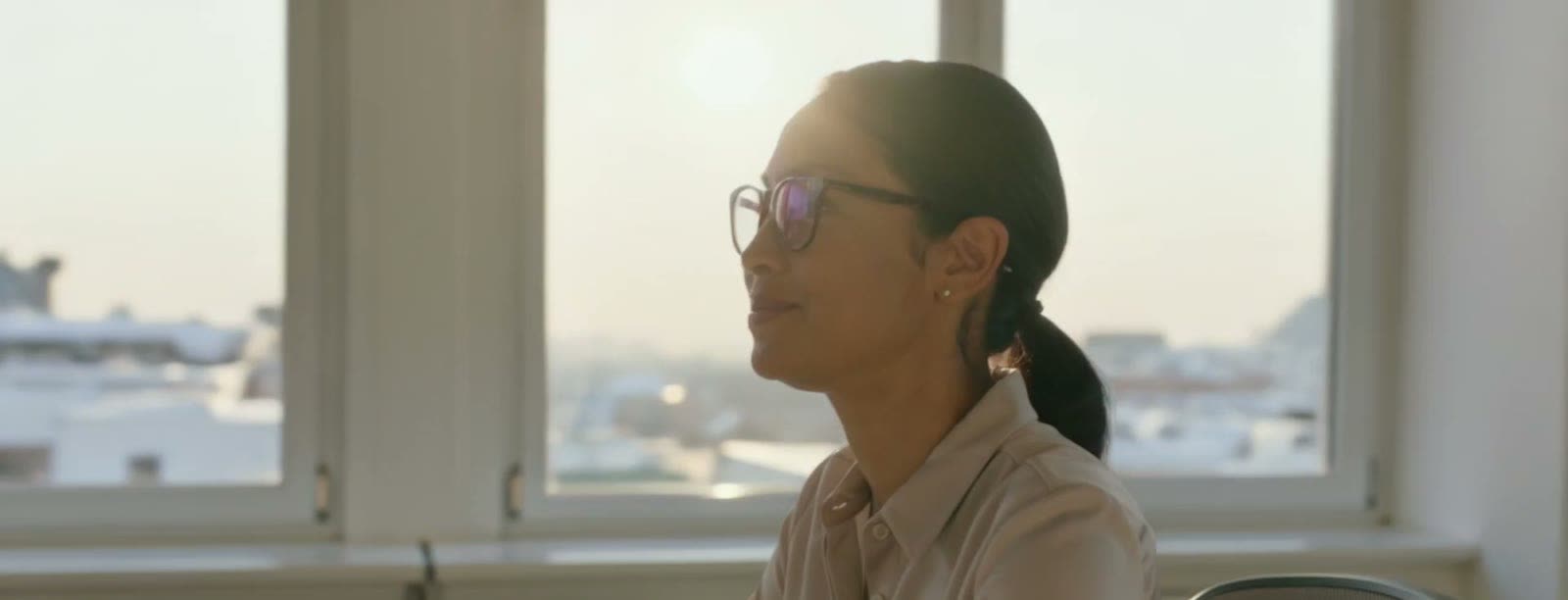 A staff member sitting at a desk by a window in the late afternoon, looking up from her work.
